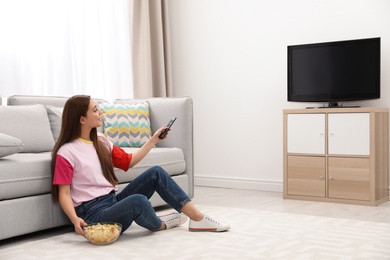 Woman with bowl of chips watching TV on floor in living room. Space for text