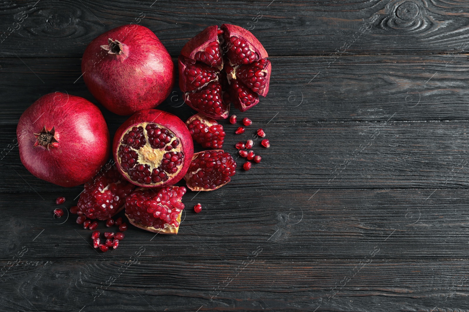 Photo of Ripe pomegranates and seeds on wooden background, flat lay with space for text