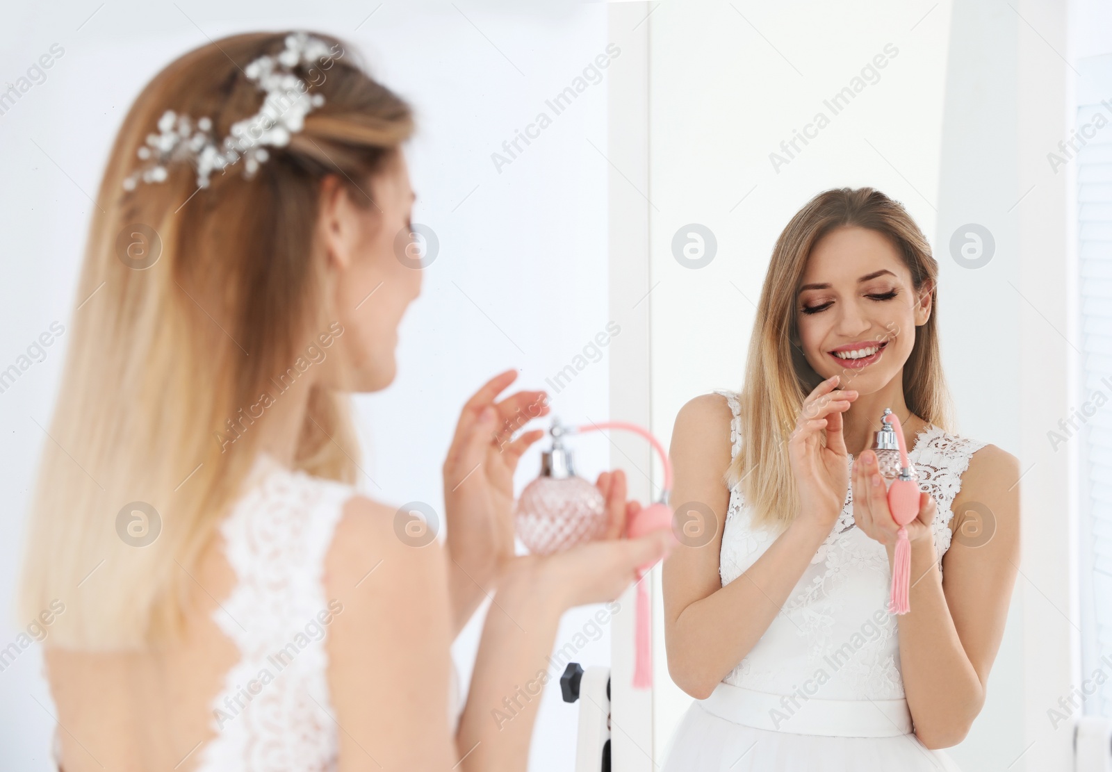 Photo of Beautiful young bride with bottle of perfume near mirror indoors