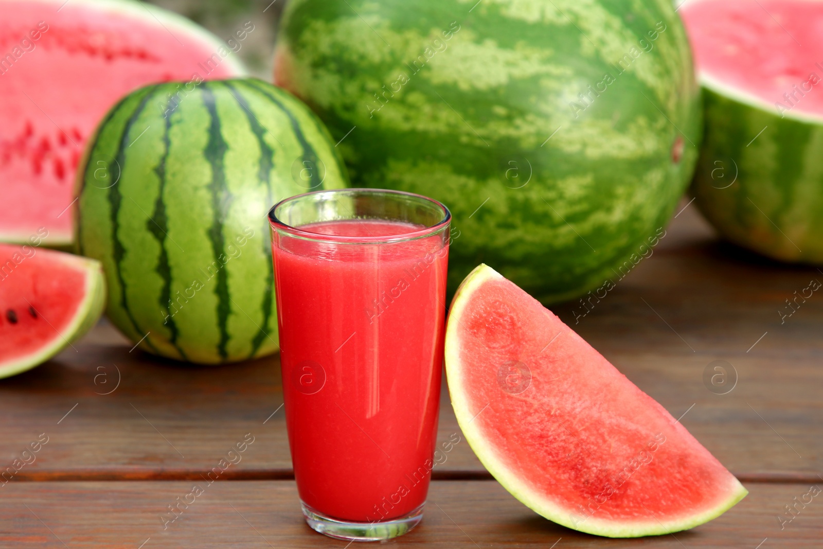 Photo of Delicious ripe watermelons and glass of fresh juice on wooden table outdoors