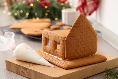 Photo of Unfinished gingerbread house and icing on wooden cutting board, closeup