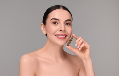 Beautiful young woman holding skincare ampoule on grey background