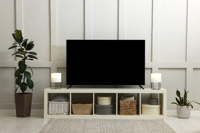 Photo of Modern TV on cabinet and beautiful houseplants near white wall in room. Interior design