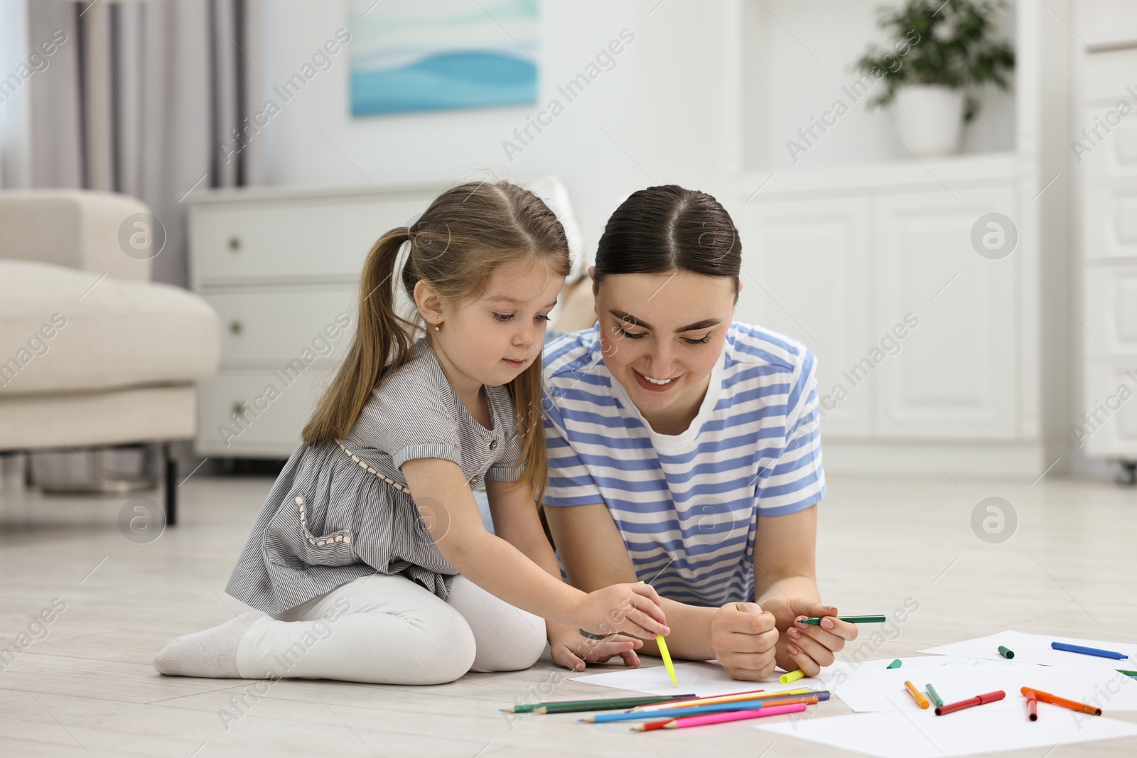 Photo of Mother and her little daughter drawing with colorful markers on floor at home