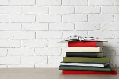 Stack of hardcover books on grey table near white brick wall, space for text