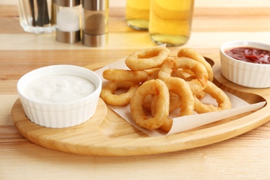 Photo of Tasty onion rings and bowls with sauces on wooden table