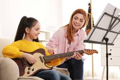 Photo of Little girl playing guitar with her teacher at music lesson. Learning notes