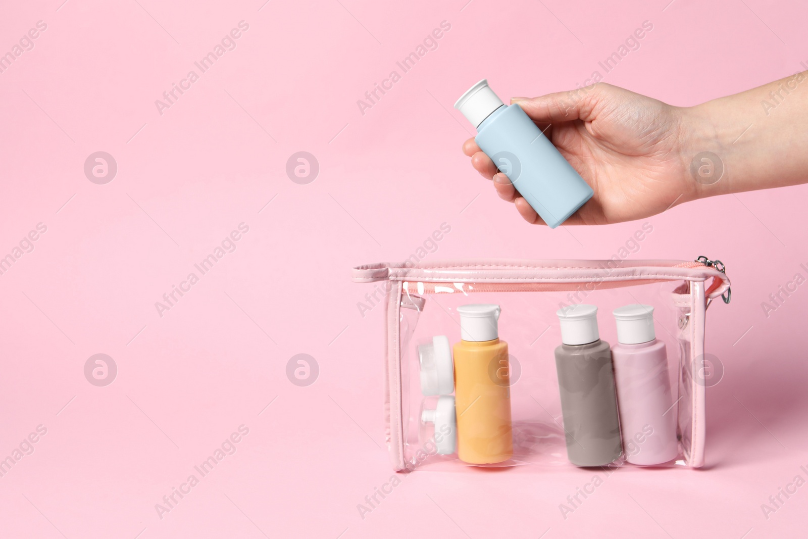 Photo of Cosmetic travel kit. Woman putting small bottle with personal care product into plastic bag against pink background, closeup. Space for text