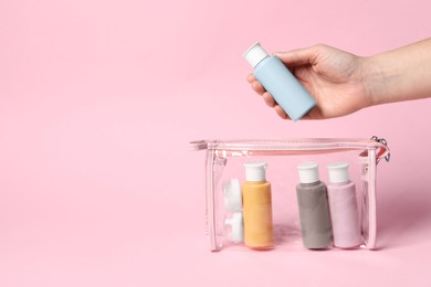 Cosmetic travel kit. Woman putting small bottle with personal care product into plastic bag against pink background, closeup. Space for text