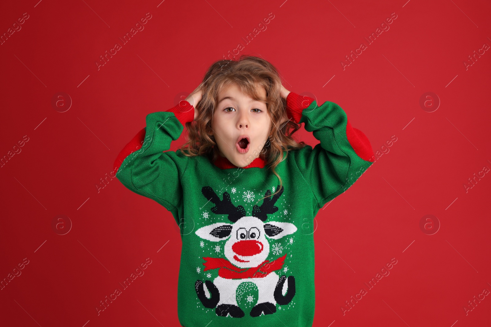 Photo of Surprised little girl in green Christmas sweater against red background