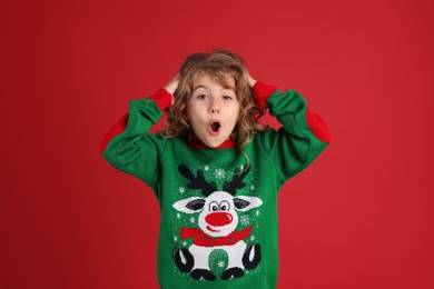 Photo of Surprised little girl in green Christmas sweater against red background