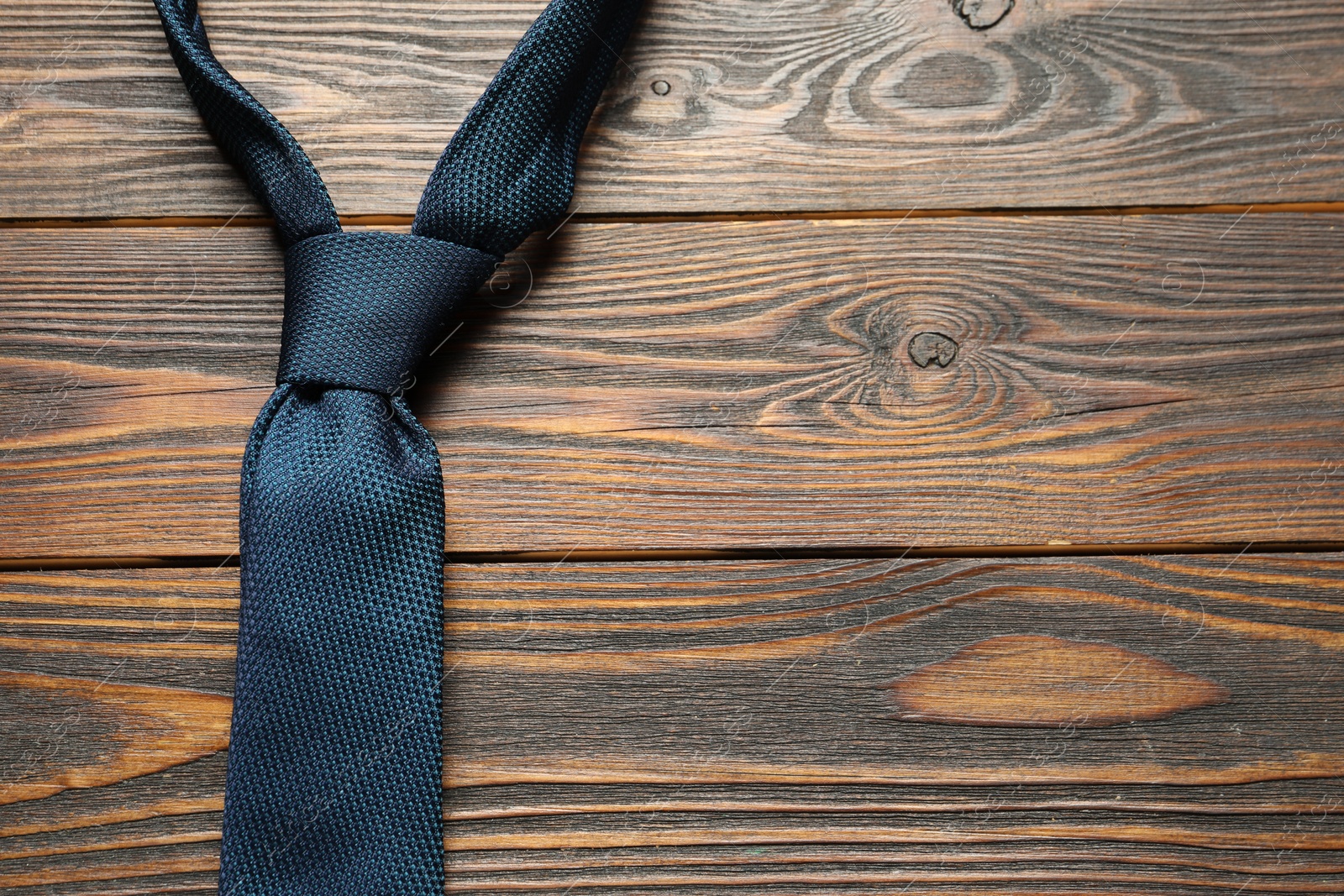 Photo of One blue necktie on wooden table, top view. Space for text