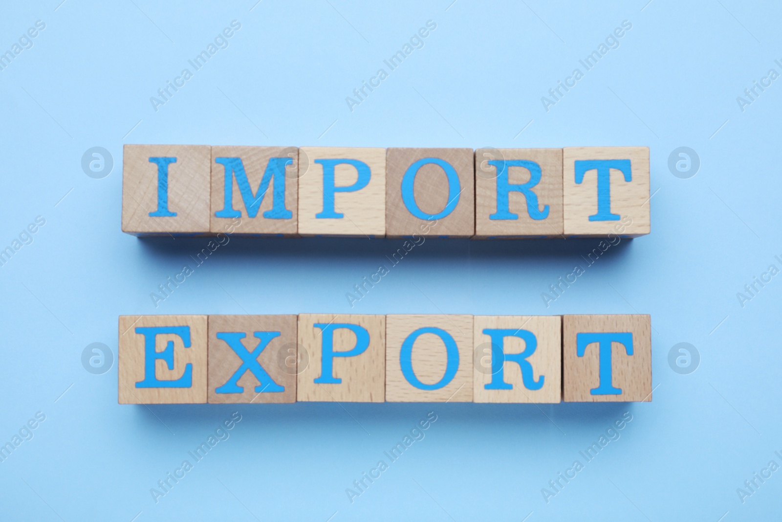 Photo of Words Import and Export made of wooden cubes on light blue background, top view