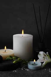 Photo of Beautiful spa composition with different care products and burning candles on dark grey table against black background