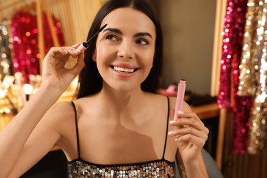 Photo of Beautiful young woman applying mascara in dressing room