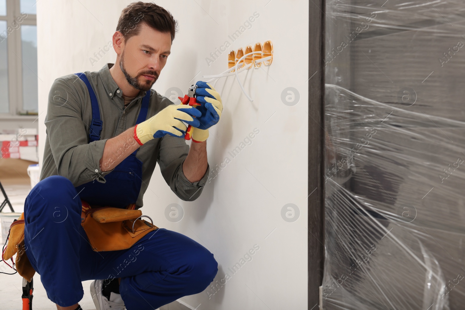 Photo of Electrician in uniform with pliers repairing power socket indoors