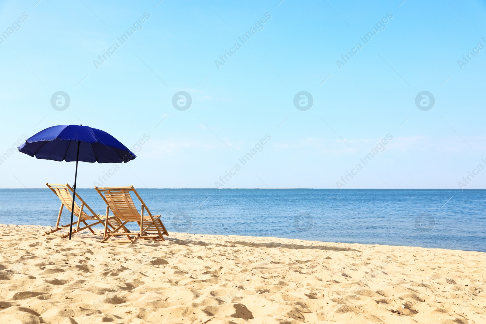 Photo of Empty wooden sunbeds and umbrella on sandy shore. Beach accessories