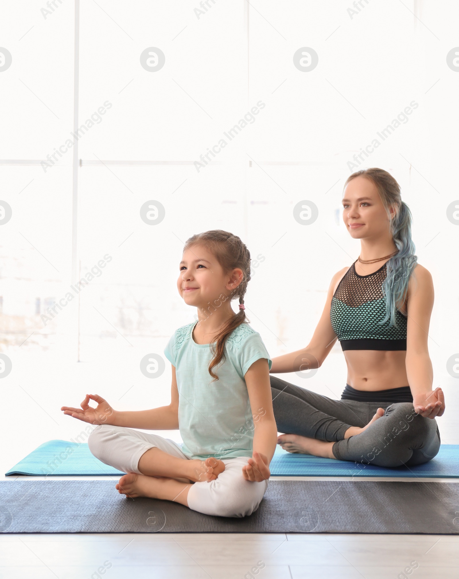 Photo of Little girl and her teacher practicing yoga in gym