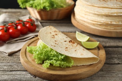 Tasty homemade tortillas, lettuce, lime and tomatoes on wooden table