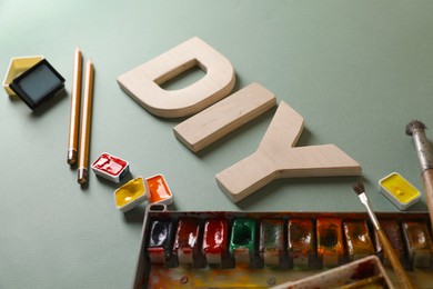 Photo of Abbreviation DIY made of letters and different painting supplies on pale green background, closeup