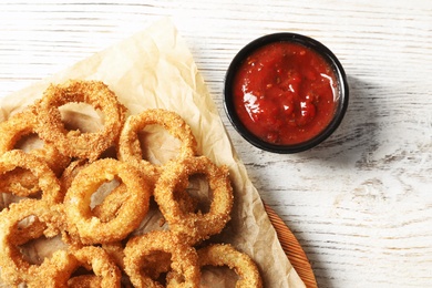 Homemade crunchy fried onion rings with tomato sauce on wooden table, top view