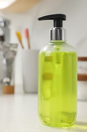 Dispenser of liquid soap on white table in bathroom