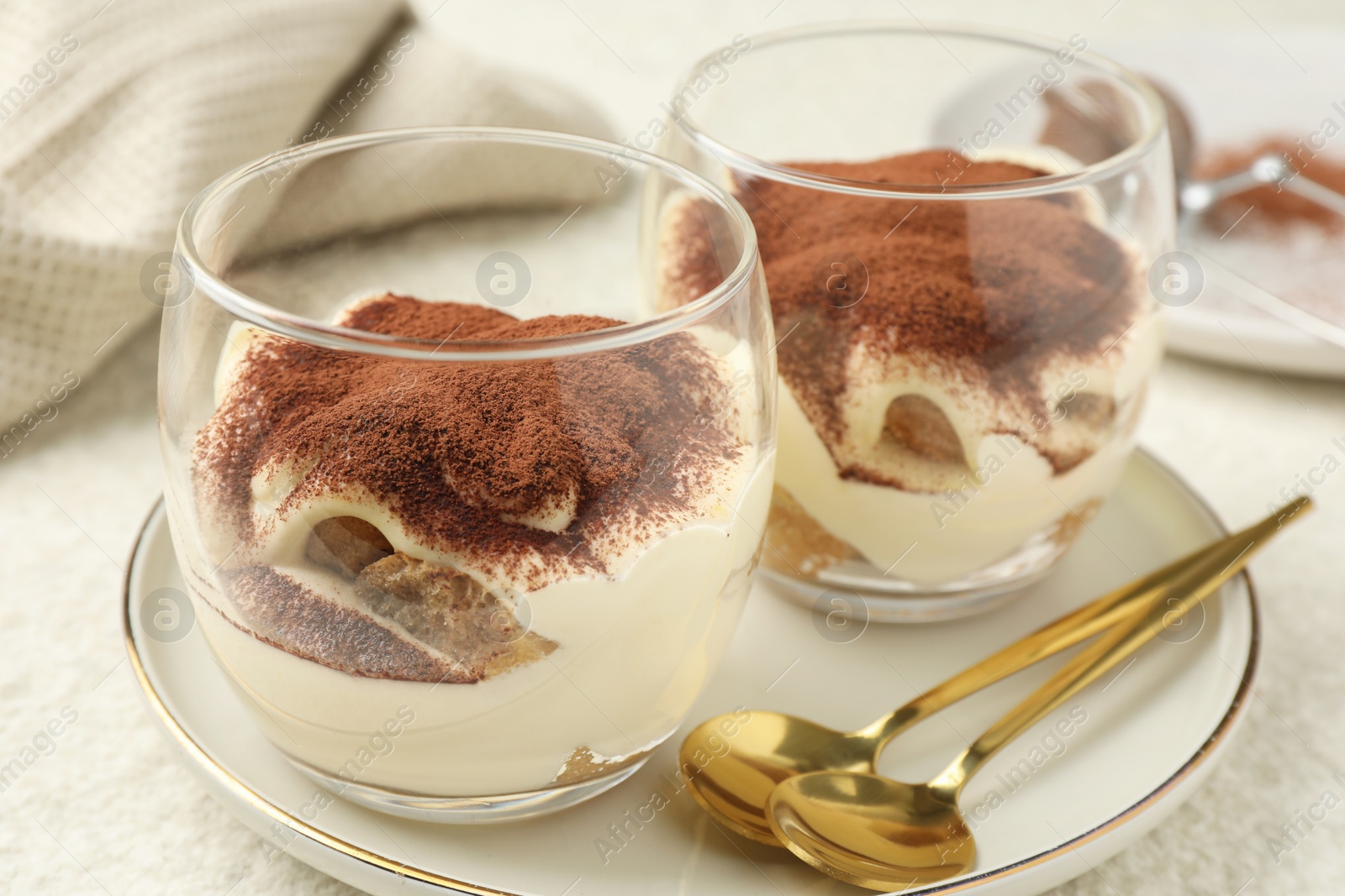 Photo of Delicious tiramisu in glasses and spoons on white table, closeup