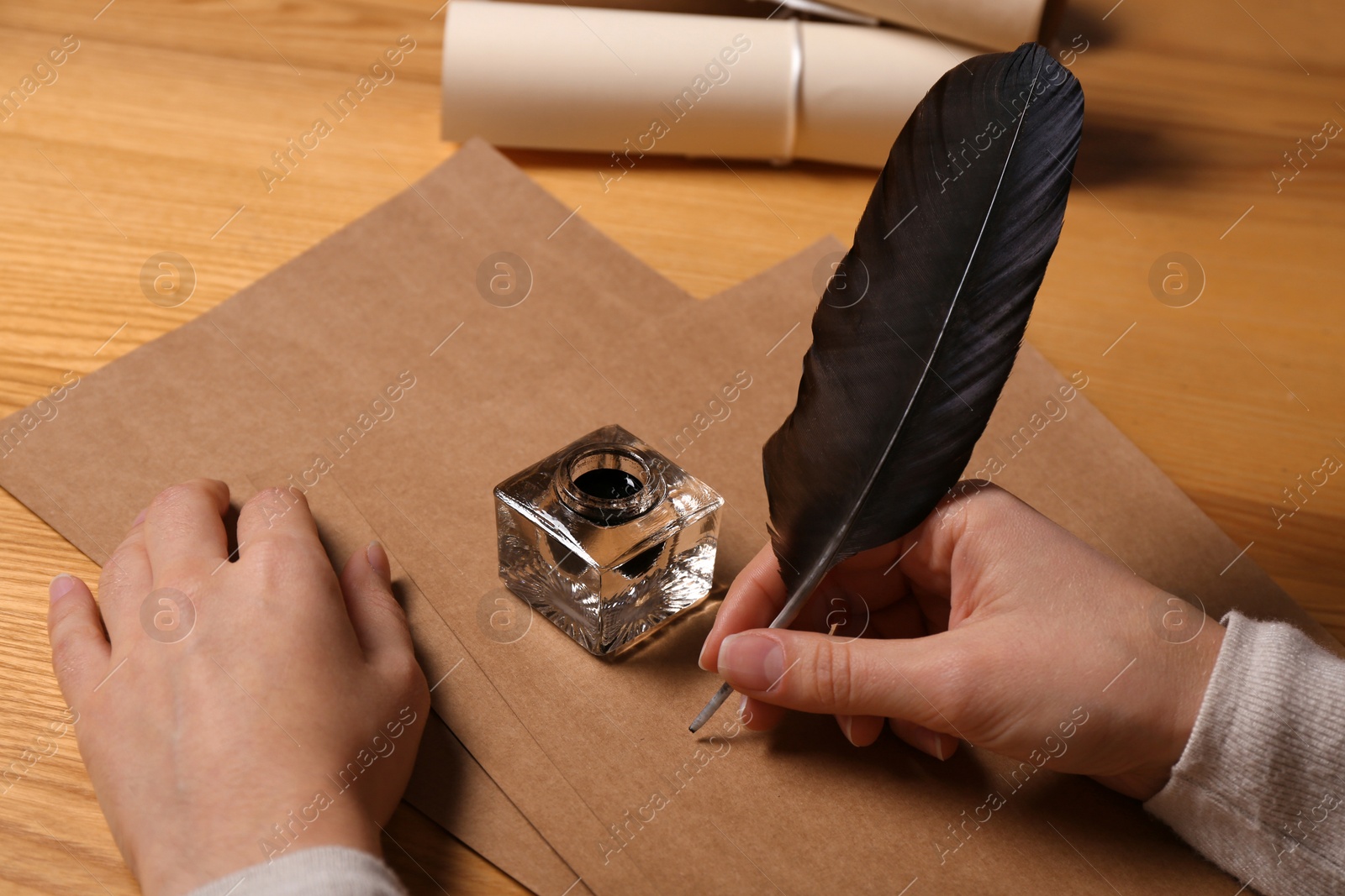 Photo of Woman using feather pen to write with ink on parchment at wooden table, closeup