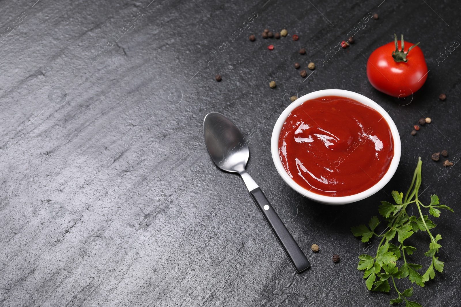 Photo of Organic ketchup in bowl, fresh tomato and spices on black table, space for text. Tomato sauce