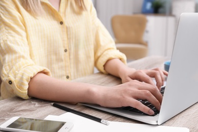 Photo of Young woman working with laptop at desk in home office, closeup