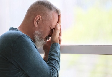 Depressed senior man near window indoors