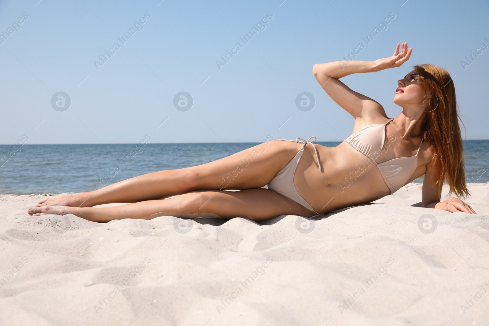 Photo of Attractive woman with perfect body in bikini lying on sandy beach near sea