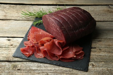 Photo of Tasty bresaola and rosemary on wooden table