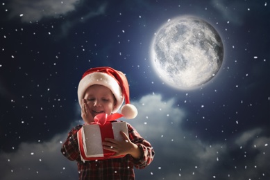 Image of Cute little boy with Christmas gift on full moon night. Waiting for Santa Claus 