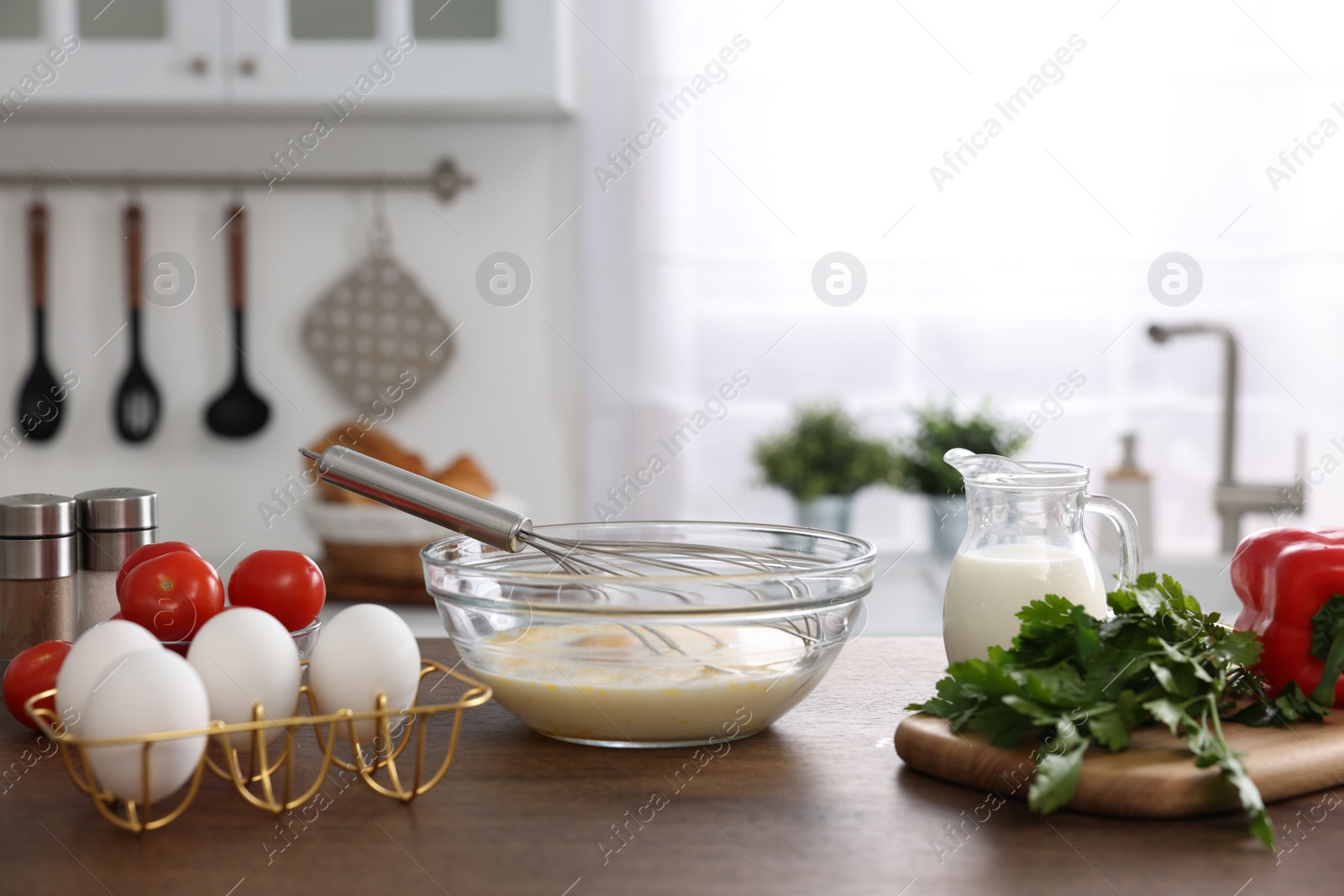 Photo of Whisk, bowl, beaten eggs and other ingredients on wooden table indoors