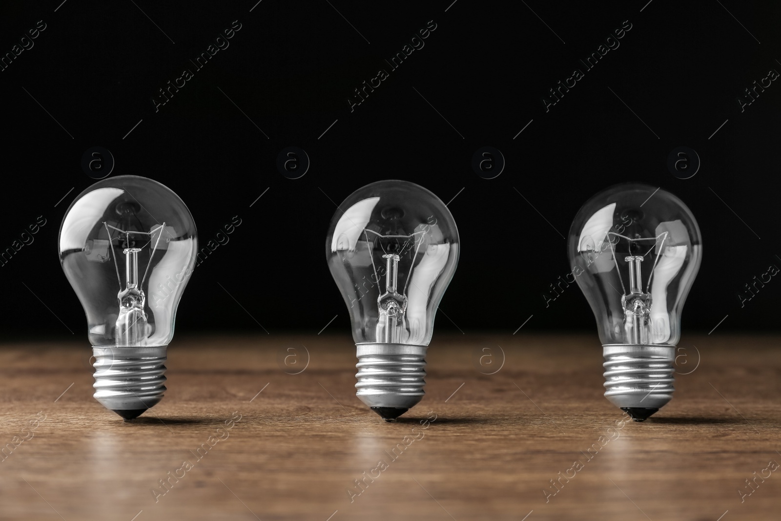 Photo of Incandescent lamp bulbs on wooden table against black background