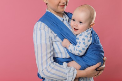Photo of Mother holding her child in sling (baby carrier) on pink background, closeup