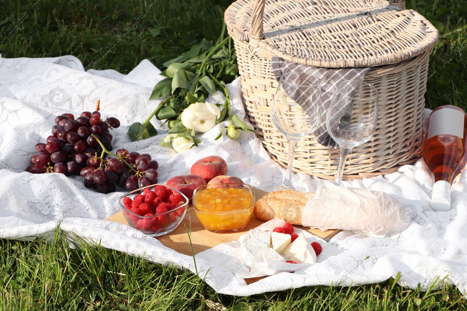 Photo of Picnic blanket with tasty food, flowers, basket and cider on green grass outdoors