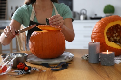 Woman making pumpkin jack o'lantern at table in kitchen, closeup. Halloween celebration