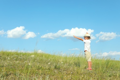 Photo of Cute little boy wearing stylish hat outdoors, space for text. Child spending time in nature