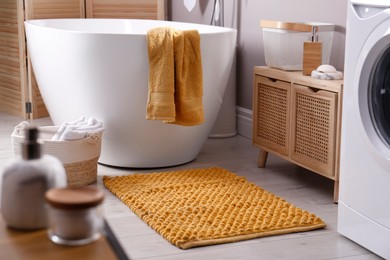 Photo of Soft orange mat on floor near tub in bathroom. Interior design
