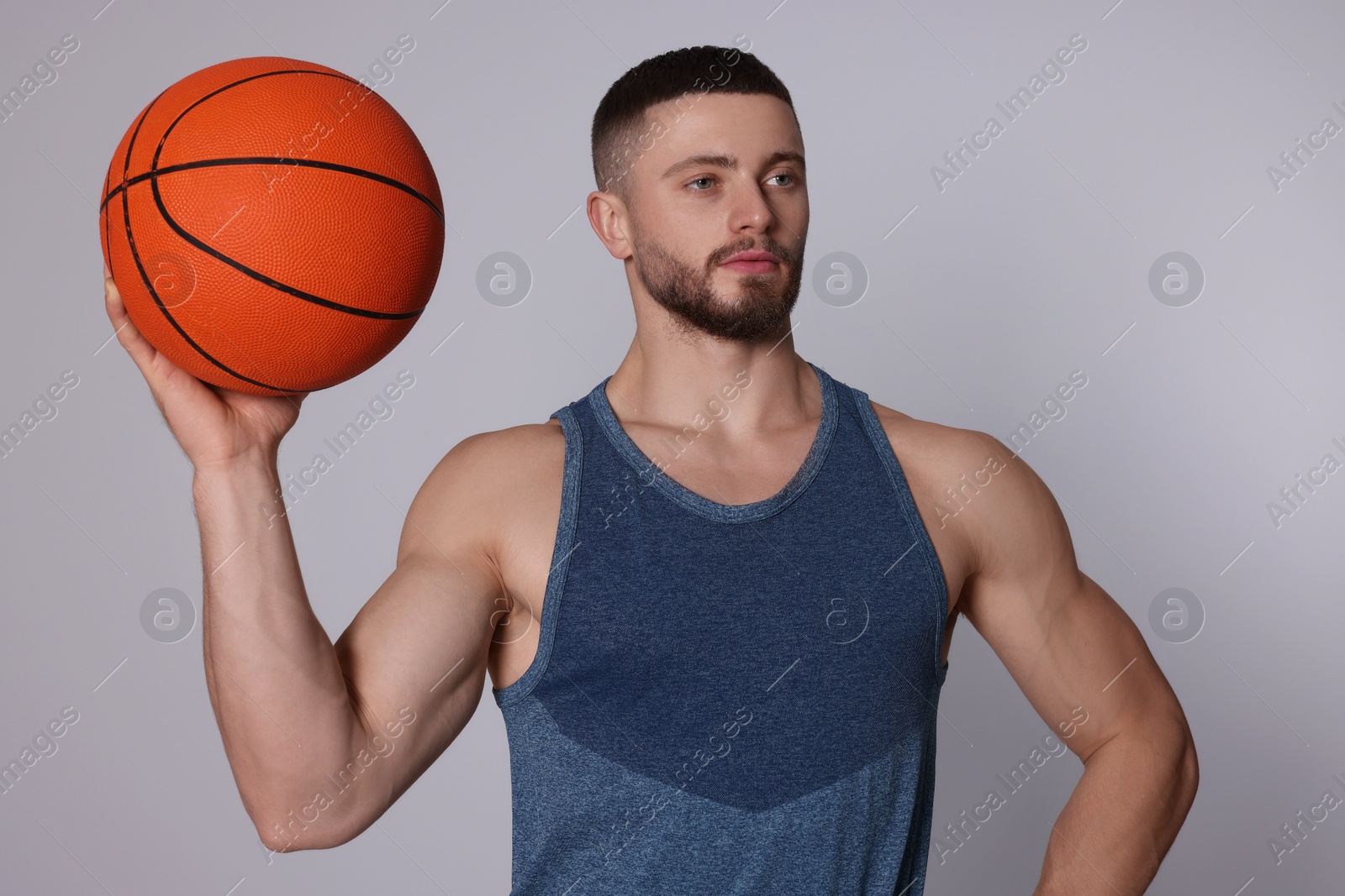 Photo of Athletic young man with basketball ball on light grey background