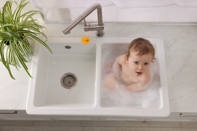 Photo of Cute little baby bathing in sink indoors, top view