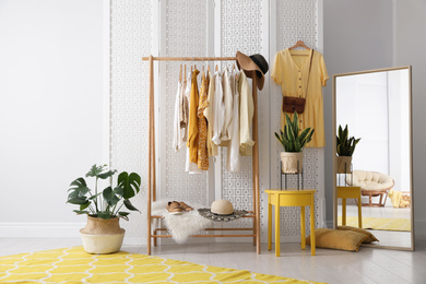 Photo of Rack with stylish women's clothes and mirror indoors. Interior design