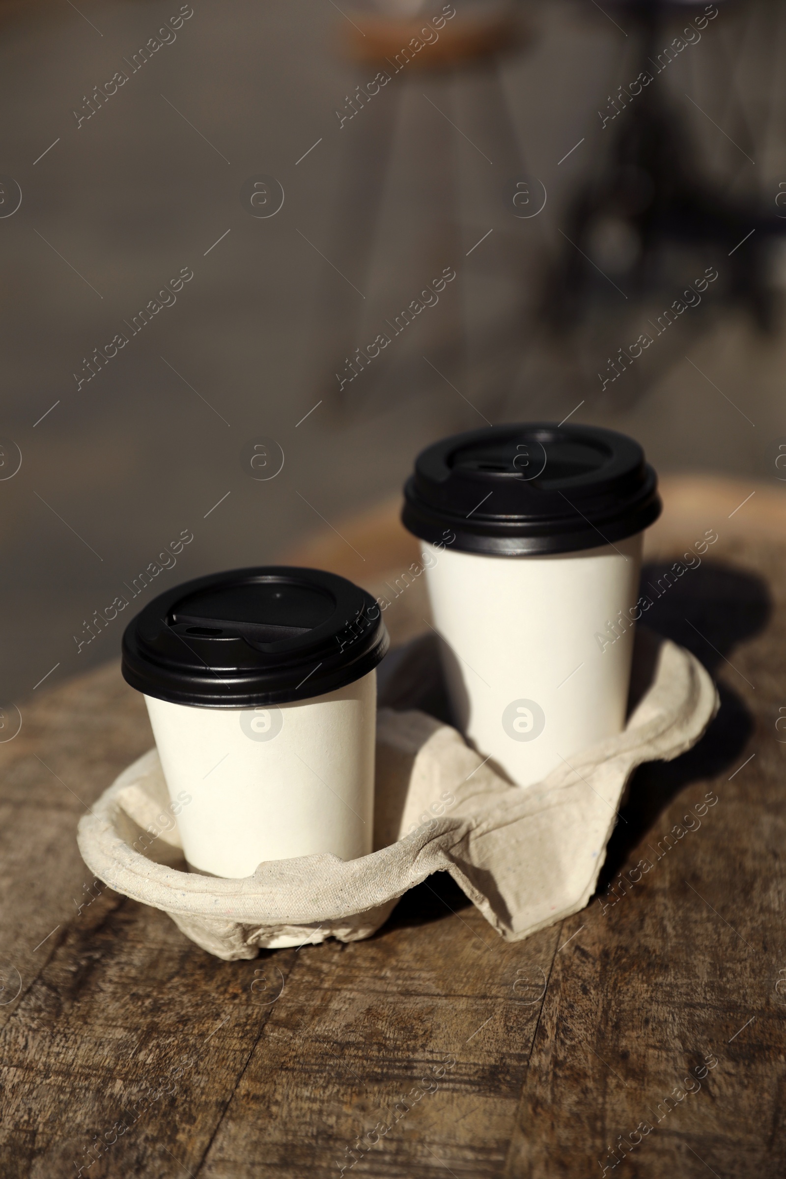 Photo of Cardboard takeaway coffee cups with plastic lids and holder on wooden table in city