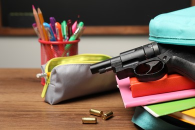 Photo of Gun, bullets and school stationery on wooden table near blackboard indoors, closeup