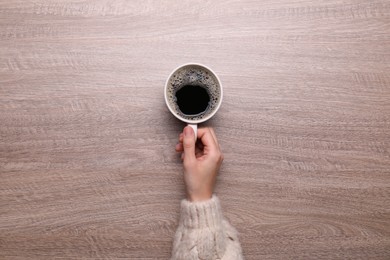 Woman with cup of coffee at wooden table, top view