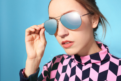 Young woman wearing stylish sunglasses on blue background