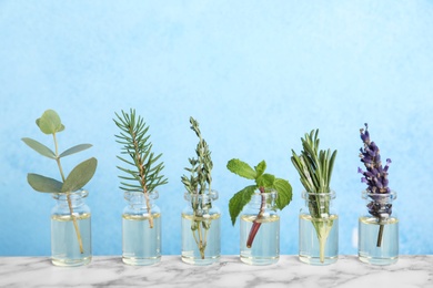 Glass bottles with different essential oils and herbs on color background