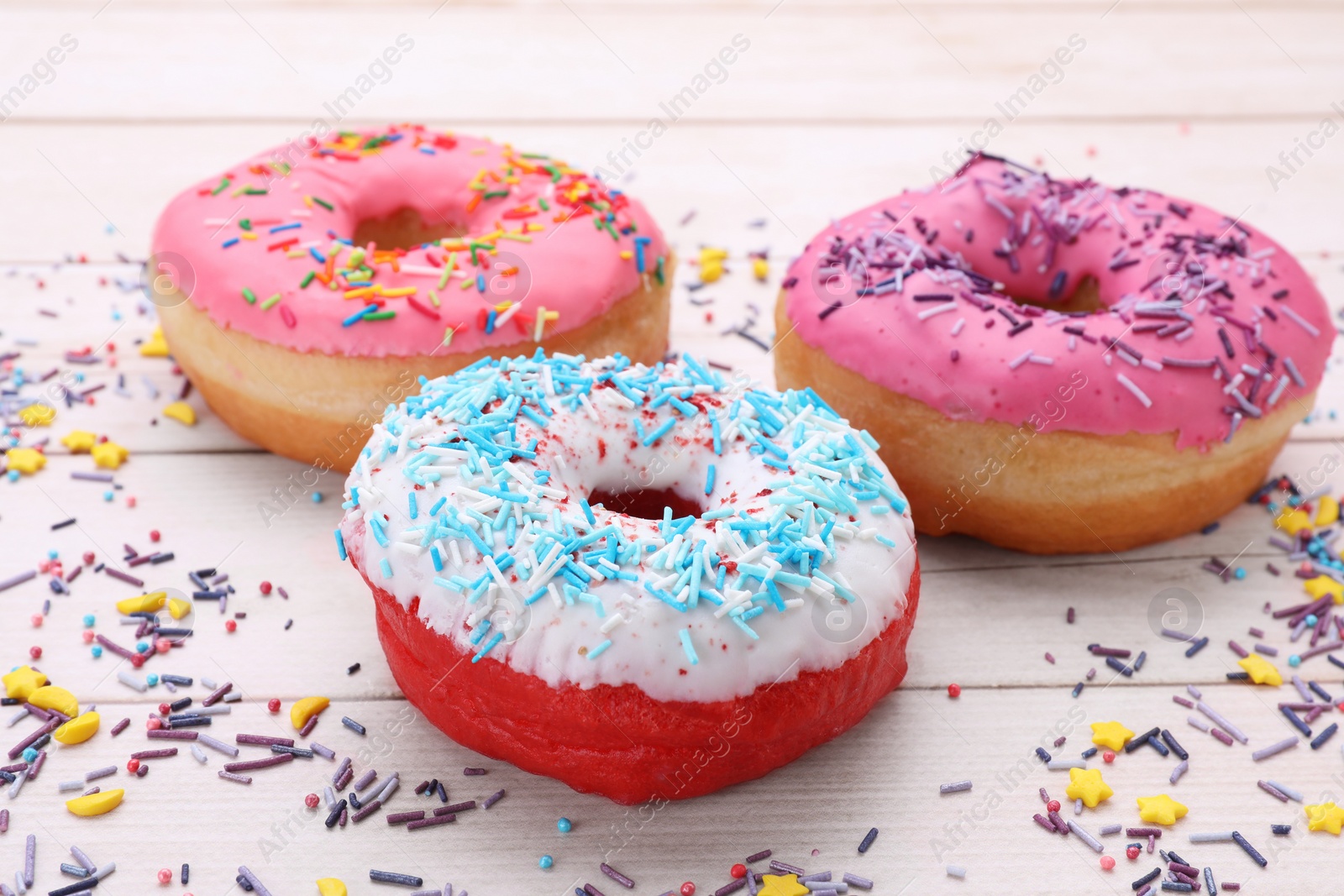 Photo of Glazed donuts decorated with sprinkles on white wooden table, closeup. Tasty confectionery